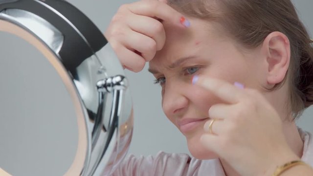 woman sad about skin imperfections. Trying to squieezing a pimple on frehead