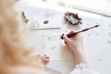 Girl writes a letter to her beloved man sitting at home at the table in a white light dress, purity...