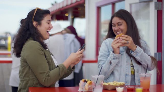 Happy Young Woman Takes Photos Of Her Fun Friend Posing With Her Burger For Social Media, They Look At The Photos And Laugh (Shot On Red Scarlet-W Dragon In 4K, Slow Motion)