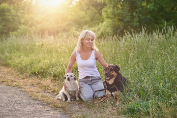 Frau im mittleren Alter sitzt mit ihren Hunden im Gras