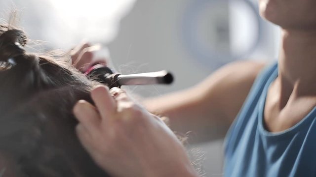 Stylist makes curly afro hairstyle for woman by hot curling hair, process of making hairstyle, hairstyles at the beauty salon