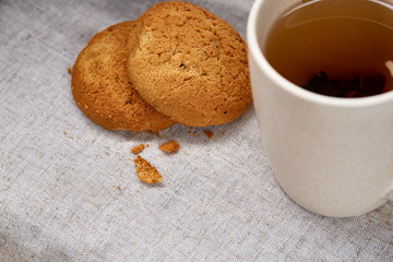 White porcelain mug of tea and sweet cookies on homespun napkin over white background, top view, selective focus