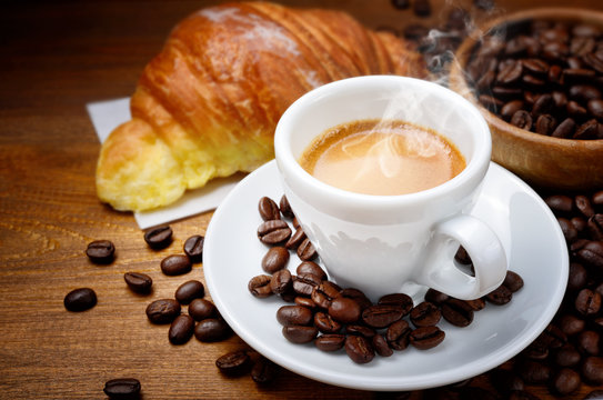 Espresso and croissant with coffee beans on wood background