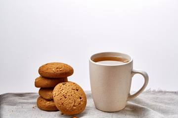 White porcelain mug of tea and sweet cookies on homespun napkin over white background, top view, selective focus
