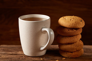 White porcelain mug of tea and sweet cookies on piece of wood over wooden background, top view, selective focus