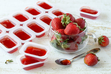 Sweet dessert. Small portioned plastic containers with berry jam and a glass mug with fresh strawberries on an old wooden table. 