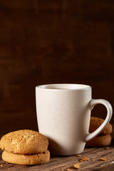 White porcelain mug of tea and sweet cookies on piece of wood over wooden background, top view, selective focus