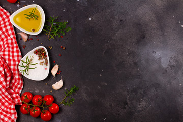 Food background - spices, olive oil and tomatoes on black stone background with copy space