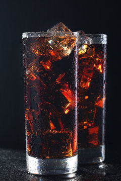 Glasses of cola with ice cubes on black stone