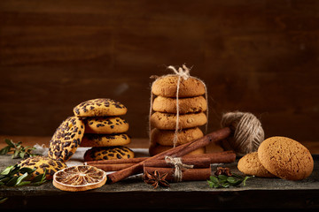 Christmas composition with pile of cookies, cinnamon and dried oranges on wooden background, close-up.