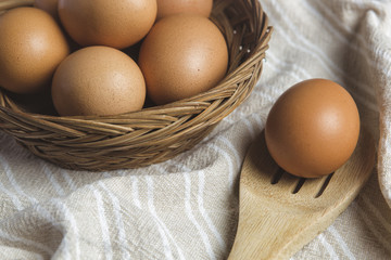 Fresh eggs in a basket, plate and spoon set, there is an egg on wood spoon on a table Cloth.