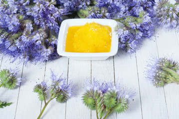 crystallized phacelia honey and flowers on white wooden background