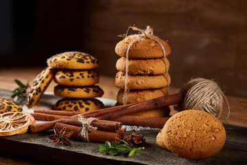 Christmas composition with pile of cookies, cinnamon and dried oranges on wooden background, close-up.
