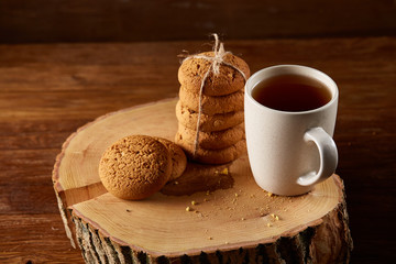 White cup of tea and cookies on a log over country style wooden background, close-up, selective focus