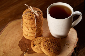 White cup of tea and cookies on a log over country style wooden background, close-up, selective focus