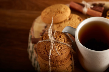 Christmas concept with a cup of hot tea, cookies and decorations on a log over wooden background, selective focus