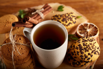 Christmas concept with a cup of hot tea, cookies and decorations on a log over wooden background, selective focus