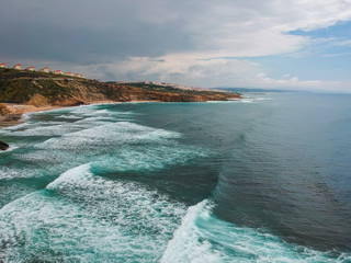 Aerial view from a surf spot with waves and a group of surfers in Ribeira d' Ilhas beach in Ericeira, Portugal