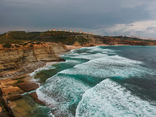 Aerial view from a surf spot with waves and a group of surfers in Ribeira d' Ilhas beach in Ericeira, Portugal