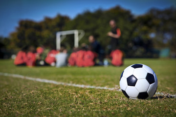 A football in foreground, soccer team and coach in background.