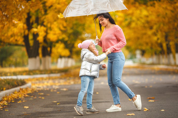 Young pretty mother with her little daughter having fun in the fall background. Happy family in...