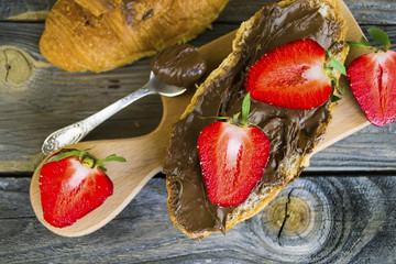 croissant with chocolate pasta and strawberries on an old wooden background
