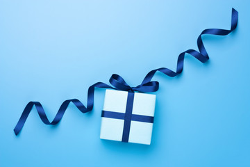 Present box with decorative bow on blue pastel surface. Flat lay. Copy space.