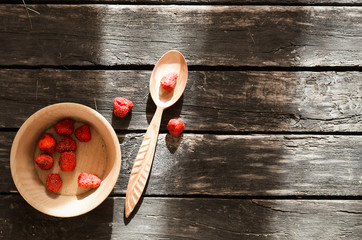 Fototapeta na wymiar Freeze dried strawberry in the wooden bowl on timber plank background.