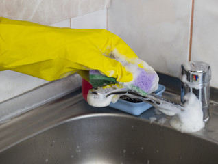 A girl in yellow gloves washes the faucet in the kitchen, close-up