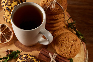 Christmas concept with a cup of hot tea, cookies and decorations on a log over wooden background, selective focus