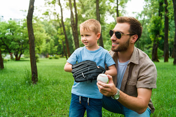 smiling father hugging son with baseball ball and glove at park