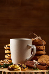 Christmas concept with a cup of hot tea, cookies and decorations on a log over wooden background, selective focus