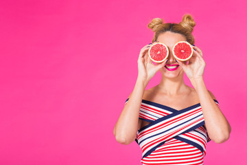 Portrait of happy girl holding halves of orange near face on pink background with copyspace