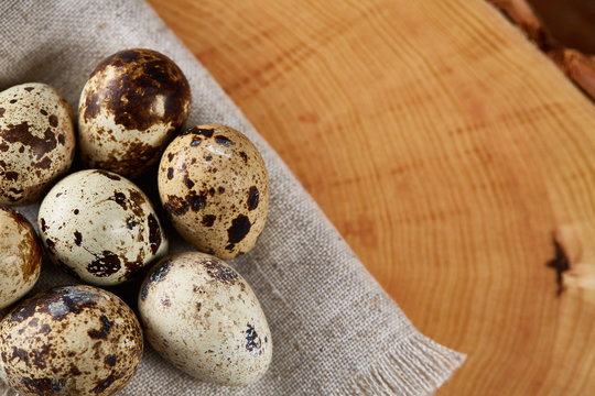 Quail eggs arranged in circle on a napkin on a log over a wooden background, close-up, selective focus.