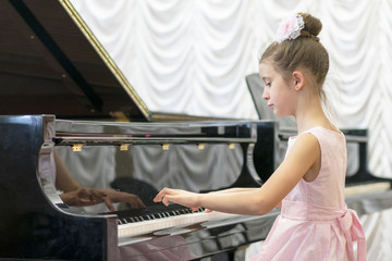 girl in a beautiful pink dress playing on a black grand piano. Girl playing on a black piano