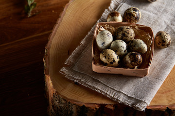 Composition of eggs quail box, eggs on a homespun napkin on a log over wooden background, top view