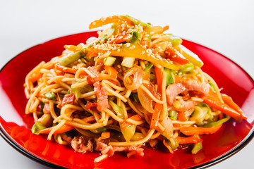 noodles with bacon, pepper and sesame seeds on a red plate on a white background. Traditional Italian pasta. Close