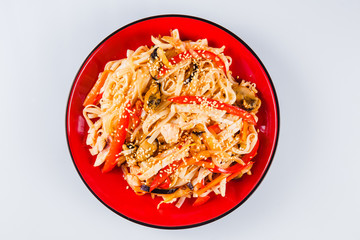 Noodles with pork, chicken, pepper and sesame seeds on a red plate on a white background. Traditional Italian pasta. Close top view