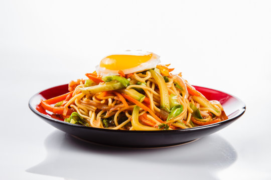 noodles with bacon, fried egg and pepper on a red plate on a white background. Traditional Italian pasta. Close