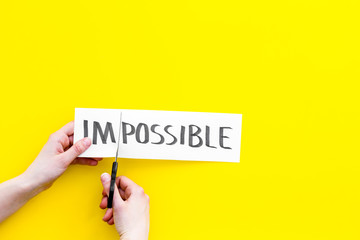 All is possible concept. Hands cutting the part im of written word impossible by sciccors. Yellow background top view copy space