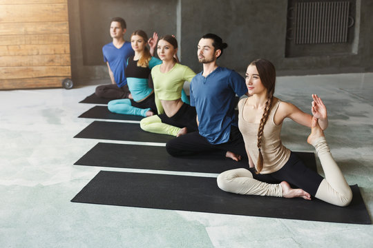 Young women and men in yoga class, mermaid pose stretching