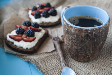 Sandwiches with sweet cheese and berries, a cup of coffee in blue wooden background