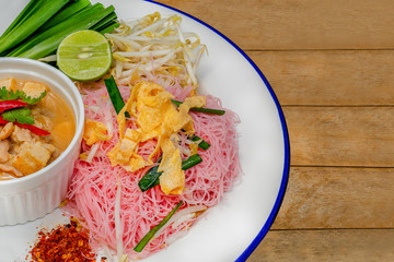 Stir Fried pink noodle with coconut milk in white dish on wooden table.Thai food and selective focus and space for texts.