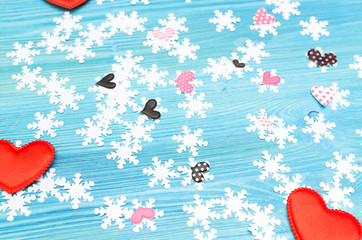 Group of differents hearts and white snowflakes on blue wooden board background.