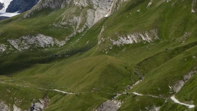 Alpine mountain side time lapse: dozens of hikers and bikers climbing and descending a mountain path while the shadows of clouds pass by.