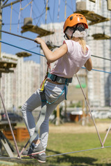 cute baby girl in climbing gear on a rope park background. Little beautiful girl climbs on rope harness in summer city park.