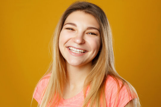 Beautiful young happy smiley woman posing in studio over yellow background