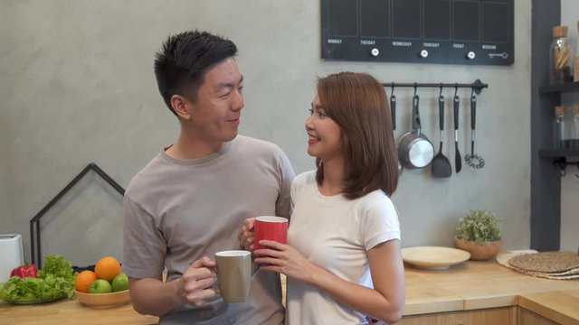 Beautiful happy asian couple are drinking a cup of coffee together in the kitchen. Man and woman talking while having breakfast. Young asian couple have romantic time while staying at home.