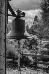 Obraz premium Bronze bell on a rusty post with a garden in the background in black and white.