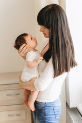side view of mother holding little infant baby in hands at home